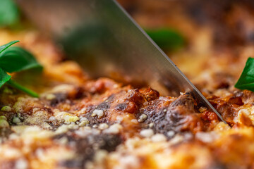 Lasagna in a baking dish according to a traditional Italian recipe is cut with a knife. Close-up.