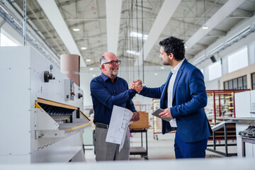 Engineers shaking hands in a factory setting, discussing strategy and growth