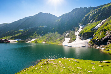 balea lake of romania. alpine landscape of fagaras mountains with pond. sunny weather with clouds on the blue sky above carpathians. snow and grass on the hillside in summer. vacation season