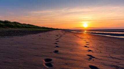 Tranquil sunset on a sandy beach with footprints leading to the water's edge