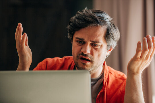 Man in red shirt looking at laptop with horror and panic during financial crisis
