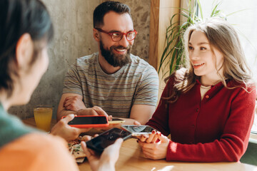 Group of smiling friends sharing content on smartphones in cafe