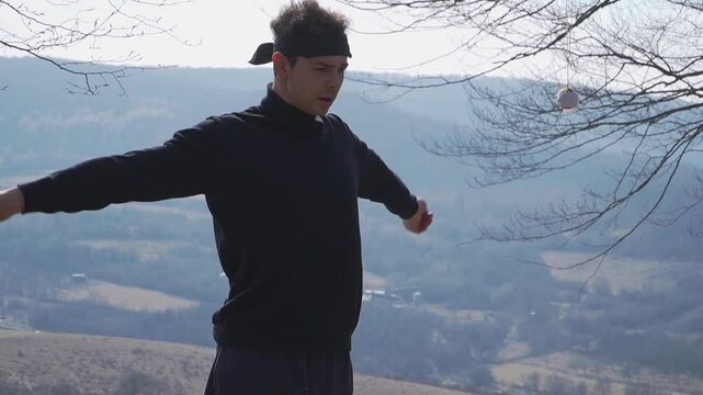 "A captivating outdoor shot of a person with arms extended, holding a tethered ball against rolling hills and trees. Ideal for sports, balance, and creative projects.