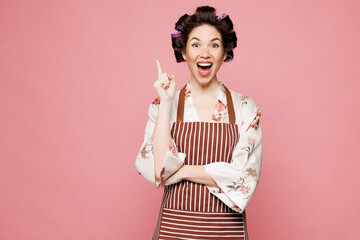 Young smart housewife housekeeper chef cook baker woman she wear brown apron holding index finger up with great new idea isolated on pastel pink color background studio portrait. Cooking food concept.