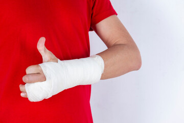 Medical Concepts. Closeup of Body Parts of Caucasian Man in Red Shirt with Broken Hand In Plaster and Bandaid Isolated on White