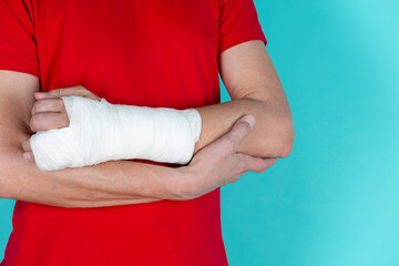 Medical Concepts. Closeup of Caucasian Man Damaged Broken Hand In Plaster and Bandaid Isolated on Turquoise Background.