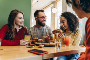 Cheerful friends eating pizza and drinking juice in restaurant