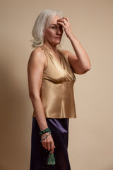 Ageing Concepts. Portrait of Senior Caucasian Blond Woman Posing in Casual Brown Blouse And Vilet Skirt In Studio Over Beige Background