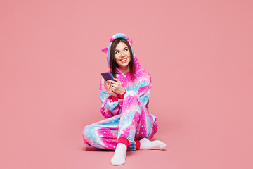 Full body young woman she wear domestic costume with hoody and animal ears sit hold using mobile cell phone look aside on area isolated on plain pastel light pink background studio Lifestyle concept