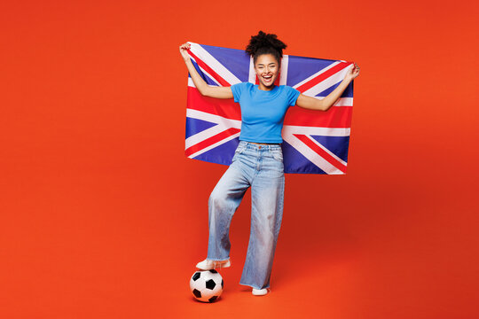 Full body young smiling woman fan wearing blue t-shirt cheer up support football sport team hold in hand British flag soccer ball watch tv live stream look camera isolated on plain orange background. - Powered by Adobe