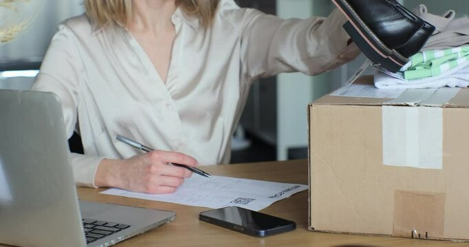 Young woman filling out a paper form, wanting to return shoes. Female writes a return order and sits at a table with a laptop at home.