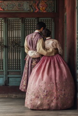 Naklejka premium Korean couple sharing a kiss in traditional attire in front of an ornate mural. Perfect for themes of romance, heritage, and Asian wedding culture.