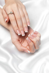Woman showing french manicure and engagement ring on white silk background