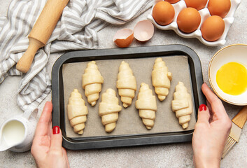 Baker placing tray of raw croissants on table before baking