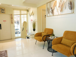 A bright waiting area with mustard armchairs and a standing mirror in front of the door.