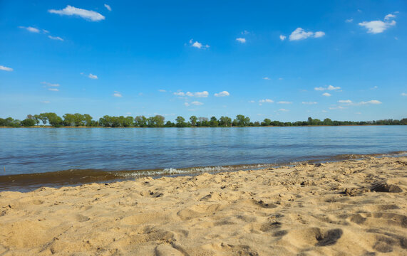 Sandsstrand am Flussufer mit B&auml;umen in der Ferne unter blauem Himmel, Weserstrand bei Oberhammelwarden, 26931 Elsfleth, Niedersachsen, Deutschland