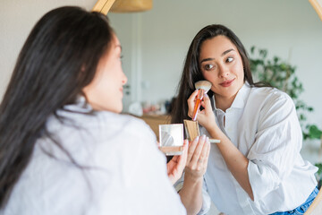 Portrait of 40 year old beautiful woman in front of mirror at home. Healthy skin. Doing her own makeup.