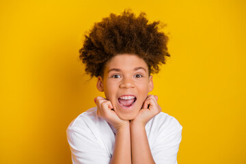 Joyful young boy with curly hair expressing excitement against a vibrant yellow background in...
