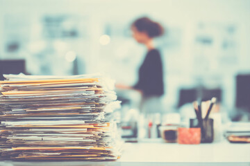 Early morning in a bright office with open desks A worker is sorting through piles of paperwork and filing them into folders