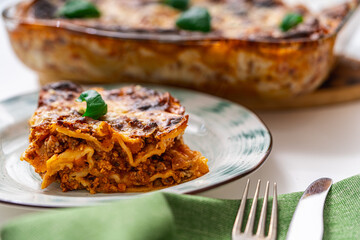 A piece of lasagna according to a traditional Italian recipe on a plate on a light background and in a baking dish. Close-up.
