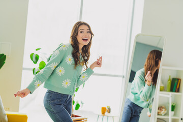 Young cheerful woman wearing a daisy-patterned cardigan enjoys a moment at home in a cozy and...