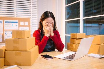 A middle-aged woman, who appears to be Asian, rests her forehead on her hand, looking stressed and...