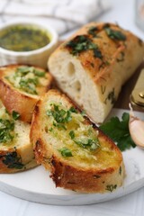 Tasty bread with garlic, herbs and oil on white tiled table, closeup