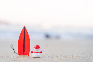 Sandy Christmas Snowman is watching the waves, standing on beautiful beach with a surf board - horizontal version in Patong Beach, Phuket, Thailand