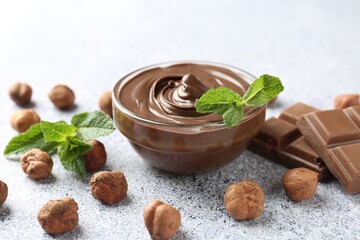 Tasty chocolate spread with mint in bowl and hazelnuts on grey textured table, closeup
