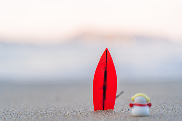 Sandy Christmas Snowman is watching the waves, standing on beautiful beach with a surf board -...