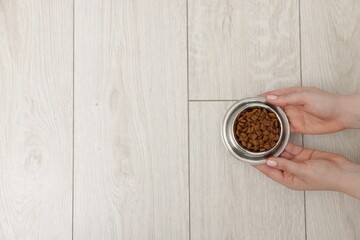 Woman with bowl of dry pet food on floor at home, top view. Space for text