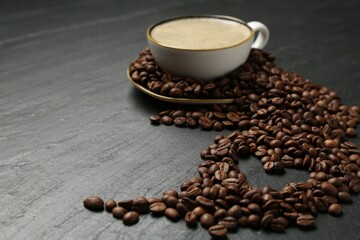 Aromatic coffee in cup and heart shaped of beans on black table, closeup. Space for text
