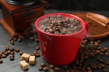 Aromatic coffee beans in cup, grinder and brown sugar on black table, closeup