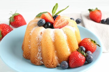 Tasty Bundt cake with powdered sugar and berries on white table, closeup