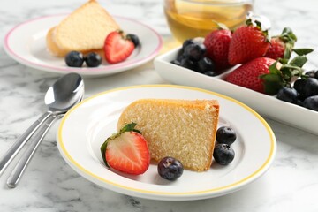 Pieces of tasty bundt cake with berries and tea on white marble table, closeup