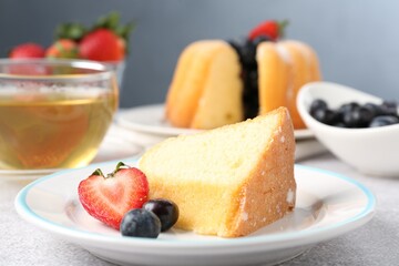 Piece of tasty bundt cake with berries and tea on light grey table, closeup