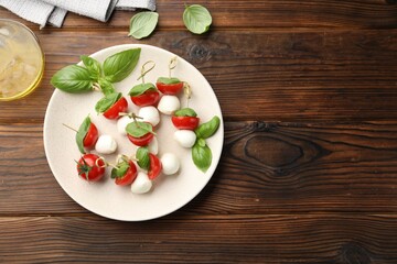 Appetizers with mozzarella, tomatoes and basil on wooden table, flat lay. Space for text