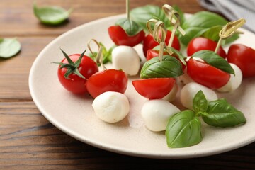 Appetizers with mozzarella, tomatoes and basil on wooden table, closeup
