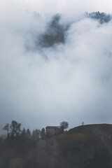 Fototapeta premium fog in the mountains on a winter day and a stone hut next to a tree