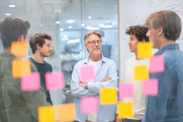 A quiet morning in an open-plan office with neutral walls A multigenerational team is gathered in front of a whiteboard, brainstorming ideas