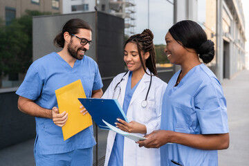 Multiracial Doctor and nurses in uniforms reviewing patient medical records outside hospital