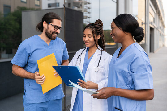 Multiracial Doctor and nurses in uniforms reviewing patient medical records outside hospital