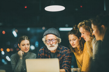  Late afternoon in an office with soft overhead lights A multigenerational team is gathered around a laptop, collaborating and discussing