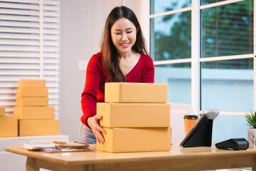 A smiling woman, who appears to be a middle-aged Asian individual, stacks cardboard boxes on a desk...