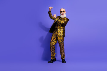 Stylish senior in a luxurious gold patterned suit and sunglasses dancing energetically against a vibrant purple background