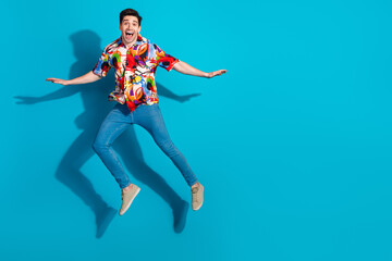 Energetic young man in colorful shirt jumping against vibrant blue background showing excitement...