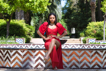 African woman, with long brown hair, young and beautiful dressed in an elegant red dress sitting...