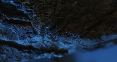 Close-up of dark rock surface with vivid blue lighting and layered texture