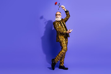 Confident Elderly Gentleman in a Glamorous Suit Posing With a Red Rose on Vibrant Purple Background