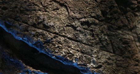 Close-up of dark rock surface with vivid blue lighting and layered texture